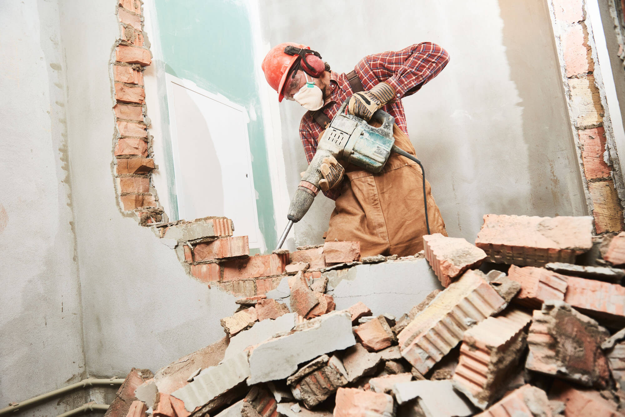 worker with demolition hammer breaking interior wall